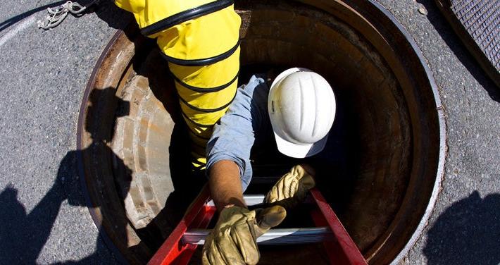 utility worker climbing down hole in street to repair underground wires